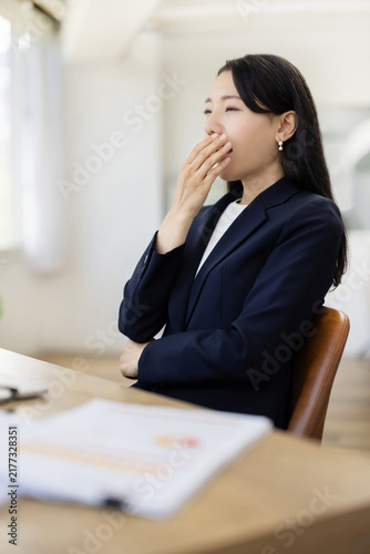Young Japanese businesswoman yawning at a desk by the window