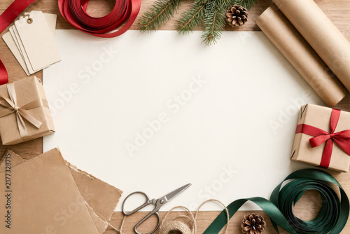 Crafting supplies and wrapped presents arranged around white paper on a wooden background