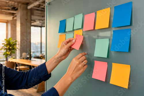 Hands Sticking Colorful Sticky Note on Glass Board in Modern Office