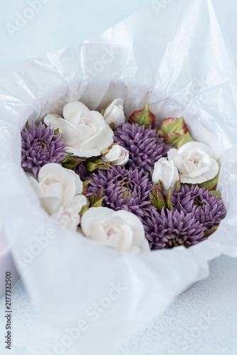 Floristry from Zephyr. White roses and purple flowers arranged in a gift box lined with tissue paper on a light blue background, perfect for special occasions