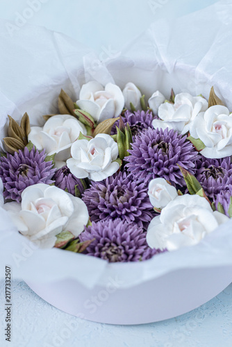 Floristry from Zephyr. White and purple artificial flowers arranged in a round white box with tissue paper, showcasing a decorative floral design for home decor or gifting