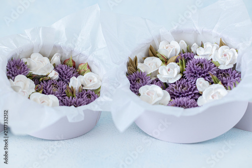 Floristry from Zephyr. Floral arrangement featuring white roses and purple asters in round boxes lined with tissue paper on a light blue background