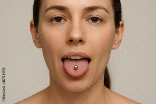 Close-up of woman with tongue piercing on neutral background