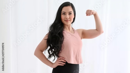 Beautiful Asian Woman Exercising at Home Instead of the Gym, Smiling and Showing Off Her Arm Muscles in a White Room While Wearing Sportswear for Fitness and Good Shape