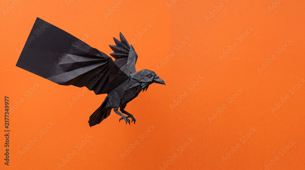 Obraz premium Origami Raven Unfolding Mid Flight, Halloween Paper Craft Object on Solid Orange Background with Copy Space