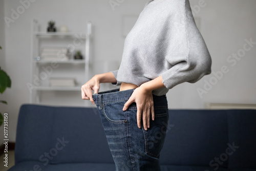 The young woman was measuring her waist with a measuring tape, taking measurements of her body. She looked at herself and saw that she had lost weight from exercising.
