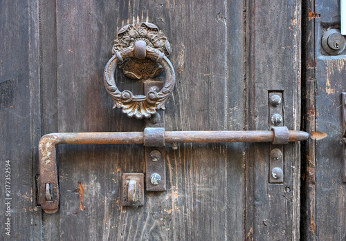 Antique iron door knocker and bolt on weathered wooden door in Verona, Italy
