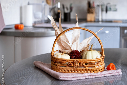 A horizontal autumn still life featuring small white decorative pumpkins in a woven wicker basket on a wooden kitchen counter with a large empty copy space for text on the left side.