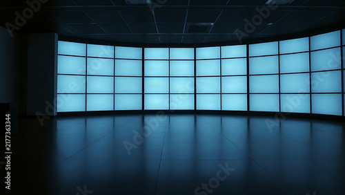 A dark control room with a wall of blank, glowing monitor screens.