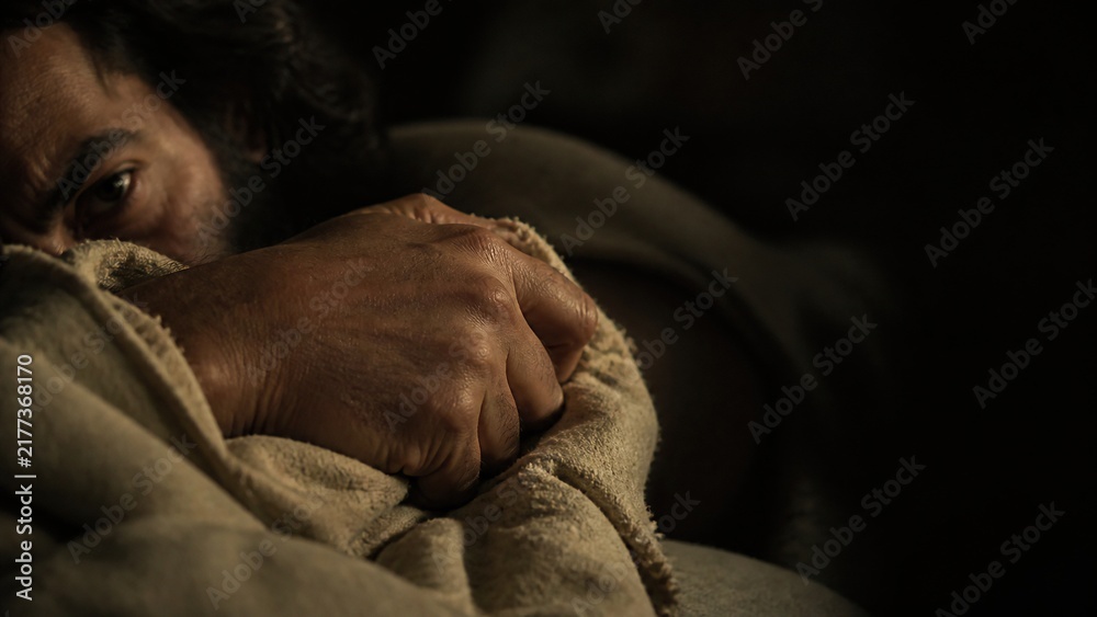 Fototapeta premium Man waking up gripping linen blanket in dark room. Bearded man opening eyes with anxiety at night. Biblical scene of Joseph awakened by angelic message, fear and faith concept