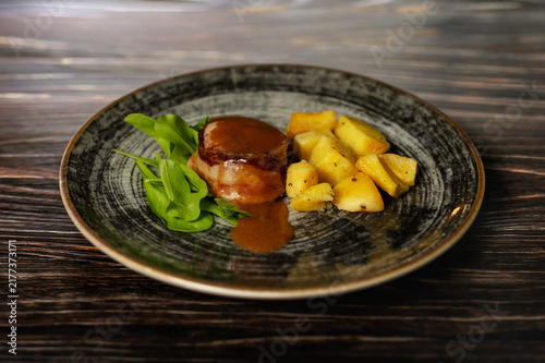 Foto Bacon-wrapped beef fillet medallion with roasted potatoes and salad in elegant r