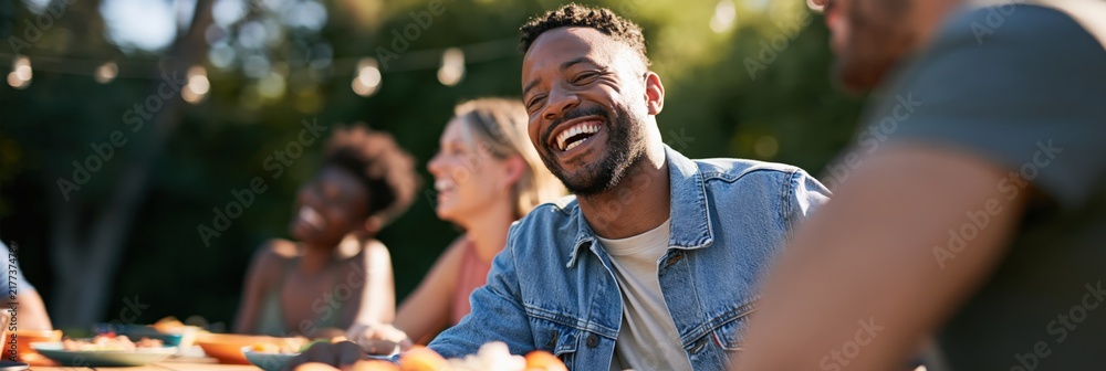 Fototapeta premium Panoramic outdoor summer picnic with diverse friends laughing and enjoying food for banner background and event promotion