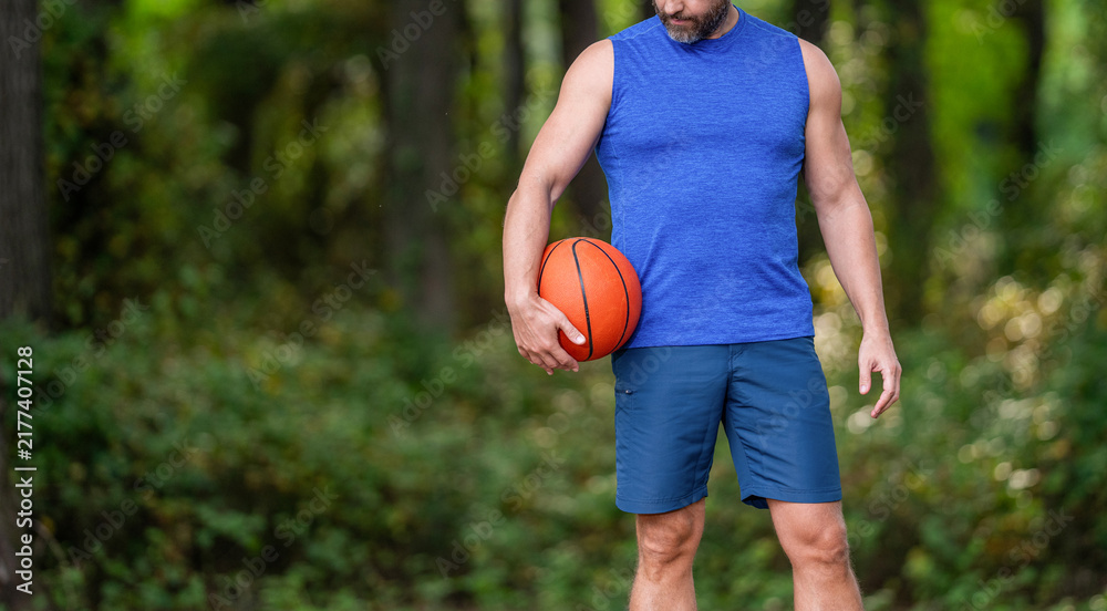 Obraz premium Guy has sport motivation, cropped view. Sport and hobby. Sport and recreation. Active lifestyle. Summer activity. Man with basketball ball in forest. Professional basketball player training outdoor