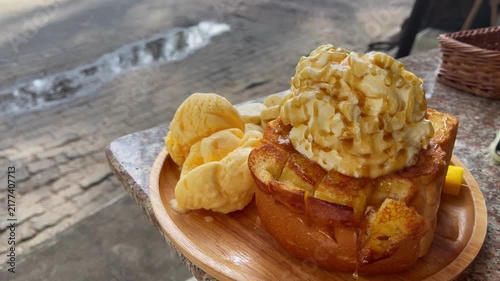 Close-up of toasted bread topped with vanilla ice cream, banana slices and whipped cream while honey is drizzled over the dessert at a café