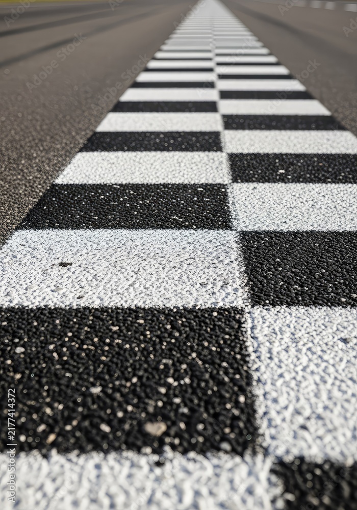 Obraz premium Ground level view of a checkered stripe painted across a professional speedway, focusing on the rough texture of the paved surface, pavement, speedway, outdoor
