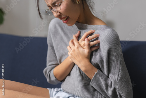 Obraz na plátně Woman clutching her chest in pain while sitting at home, representing chest discomfort, sudden pain, health emergency, illness symptoms, cardiovascular health, medical care, patient awareness