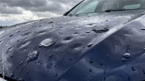 Severe Hail Damage Dents and Melting Ice Stones on Dark Blue Car Hood