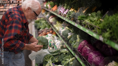 Canvas Print An elderly man is shopping for vegetables in a grocery store, focused on picking