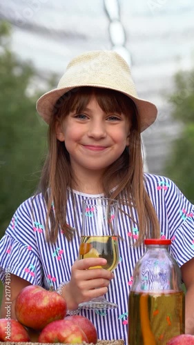 Blue-Eyed 12-Year-Old Girl Smiling While Drinking Homemade Apple Juice. Happy girl enjoying natural homemade juice in an apple orchard during harvest.