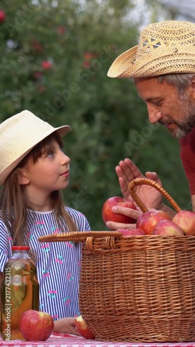 Father and Daughter Discuss Homemade Apple Juice in Apple Orchard. Farmer father explaining how fresh apples become healthy homemade juice while bonding with his daughter.