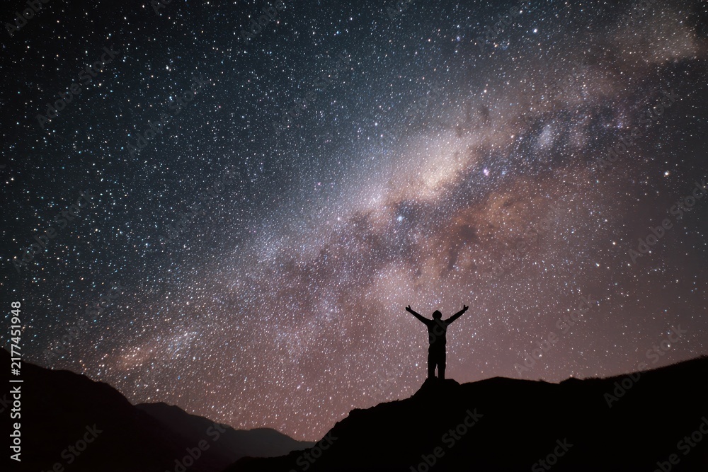 Fototapeta premium Silhouette of a person standing on a mountain peak looking at the milky way galaxy and starry night sky with milkyway silhouette mountain astronomy stargazing universe exploration