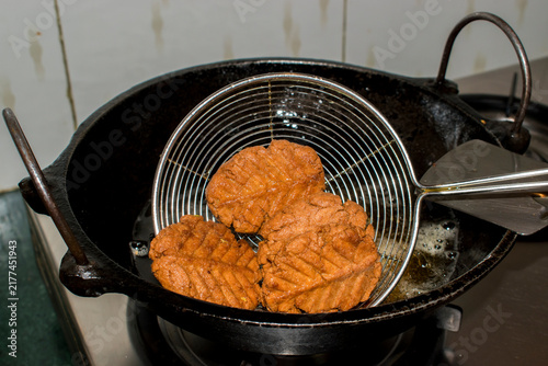 Foto lifting freshly fried thekua from hot ghee with strainer, showing a traditional step in Chhath Puja sweet preparation