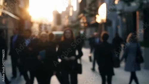 Intentionally blurred business professionals walking along a sunlit urban sidewalk between commercial. Business presentations, corporate recruitment, and financial services advertising.