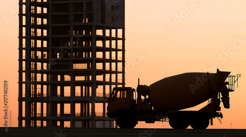 Silhouette of a concrete mixer truck parked in front of an unfinished high-rise building under a warm golden sunset sky backdrop