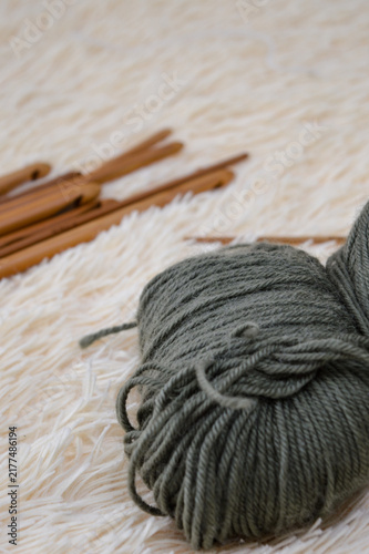 Obraz na płótnie Balls of olive green wool yarn resting on a soft white fluffy fur surface with wooden crochet hooks blurred in the background