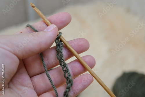 Woman hand holding a wooden crochet hook working on a green wool yarn chain close-up. Crocheting process, handmade yarn craft, needlework project, and cozy hobby concept