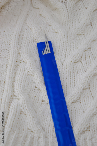 Set of double-pointed metal knitting needles in a blue plastic package resting on a white knitted woolen sweater close-up. Knitting supplies, needlework equipment, craft tools, and cozy hobby concept