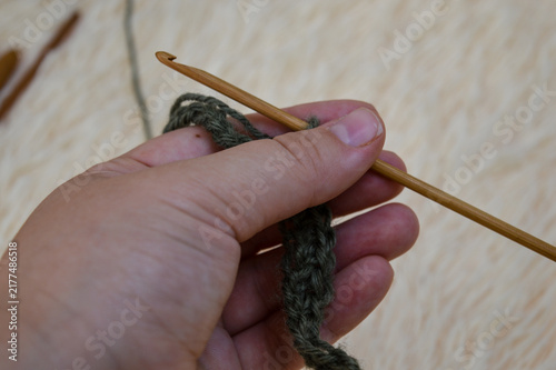 Woman hand holding a wooden crochet hook working on a green wool yarn chain close-up. Crocheting process, handmade yarn craft, needlework project, and cozy hobby concept