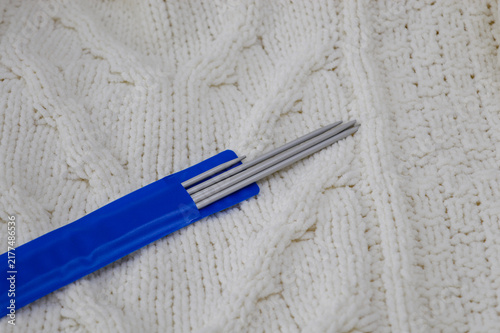 Set of double-pointed metal knitting needles in a blue plastic package resting on a white knitted woolen sweater close-up. Knitting supplies, needlework equipment, craft tools, and cozy hobby concept