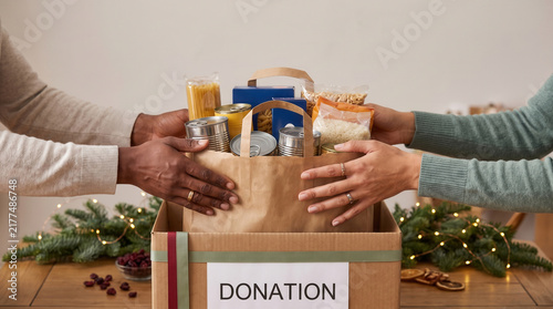 Hands placing food in a donation box during christmas food drive. community support and holiday charity concept