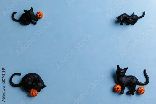 Flat lay composition with black cat figurines and small orange pumpkins on a light blue textured background for halloween