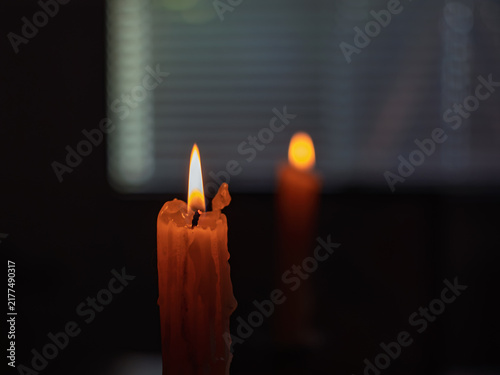 Картината върху платно Two lit candles burn brightly indoors set against window blinds