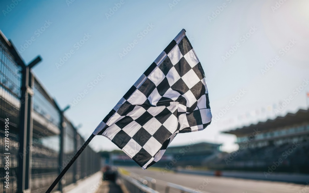 Obraz premium Black and white checkered racing flag waving at a racetrack