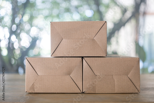 Three of square cardboard boxes are piled on wood table. Show the bottom box