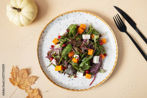 Plate with salad with greens, pumpkin and soft cheese on beige background top view, flat lay