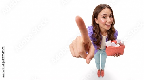 Young woman pointing at camera while holding a cosmetic makeup bag on white background