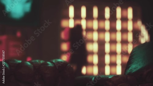 A soft brown couch sits in a well lit room. Colored lights create patterns on the wall. The scene has a relaxed atmosphere. There are shadows and warm tones in the background.