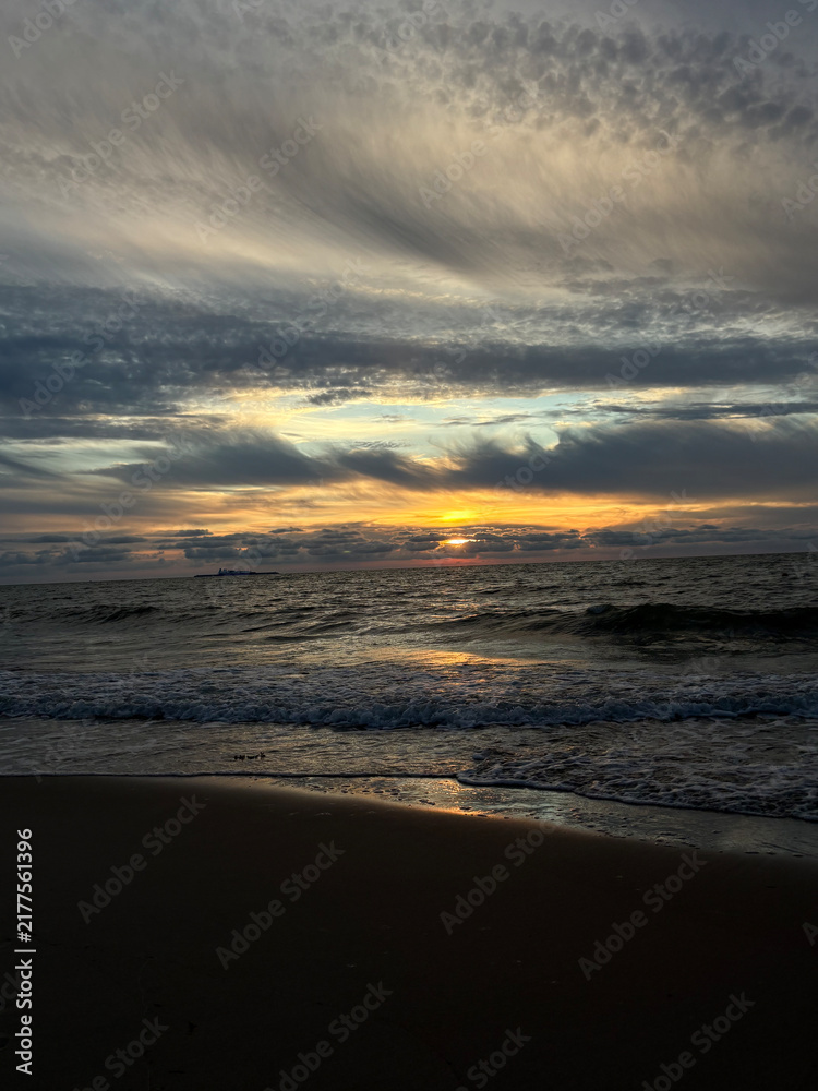 Fototapeta premium Dramatic golden sunset over stormy sea waves with flying seagull and expressive clouds