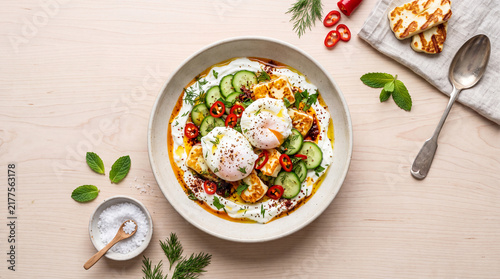 Top view of a fresh healthy breakfast bowl with yogurt, granola, fruit and herbs served on a wooden table with spoon and napkin.