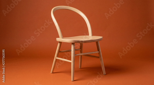 Simple modern wooden chair with a curved backrest standing against a warm orange studio background, creating a clean minimalist interior and furniture concept.