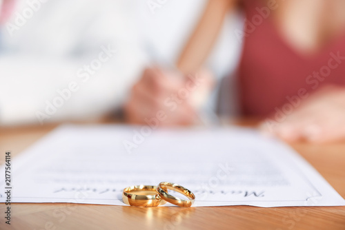 Bride signing marriage contract at wooden desk, focus on engagement rings