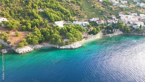 Drone view of an Adriatic coastal town with turquoise sea, green hills and a beach.