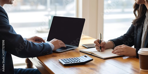 Business colleagues working together at a wooden office desk with a laptop, calculator, notebook, and coffee cup near