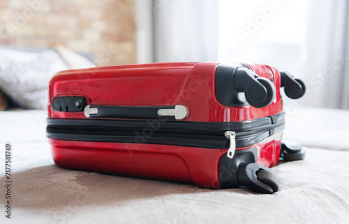 Red Carry-On Suitcase Sitting On A Bed As Sunlight Streams Into The Hotel Room