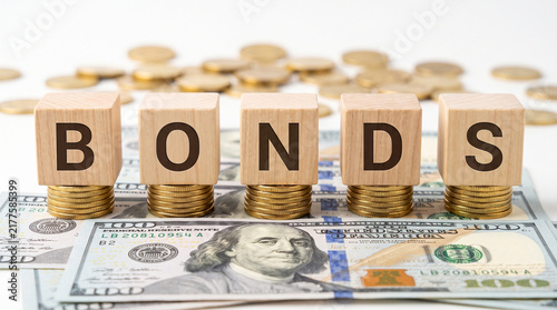 Bonds investment concept with wooden blocks on gold coins, US dollar bills representing financial security and wealth growth isolated on White Background