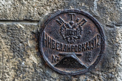 Foto A close-up of a rusty round metal geodetic marker (Nivelivka) from 1912, Russian Empire, embedded in an old brick wall